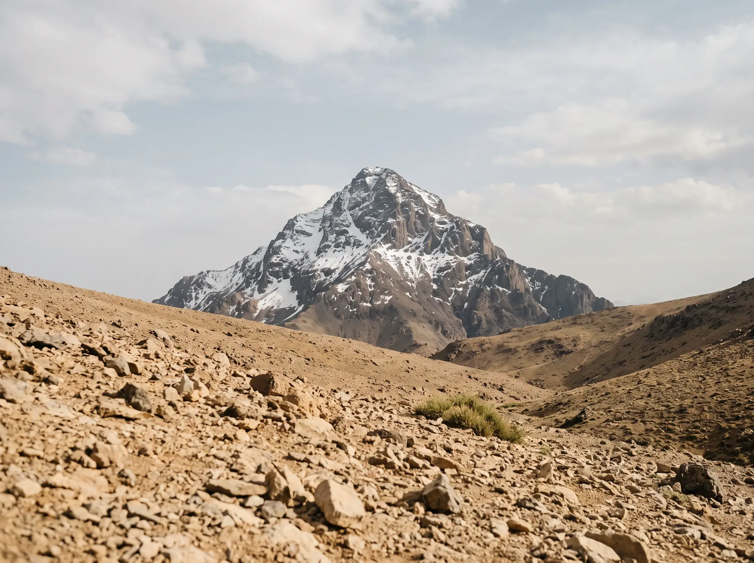 Un sommet isolé du Haut Atlas en lumière d'après-midi, neige sur le tiers supérieur, éboulis ocre au premier plan.