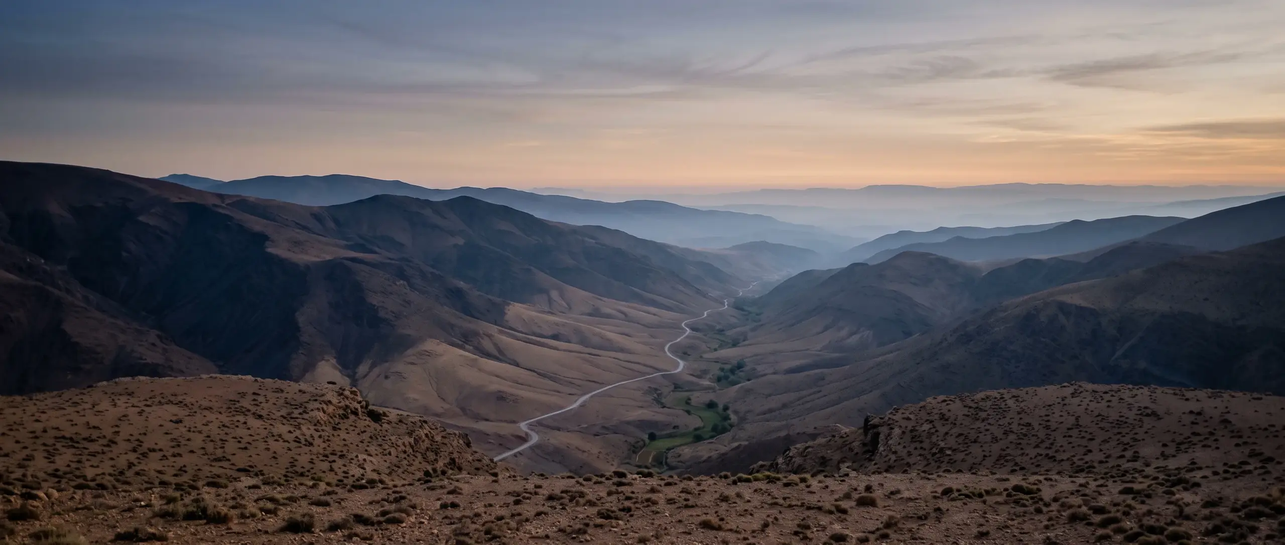 Les contreforts de l'Atlas au petit matin, crêtes superposées s'effaçant dans la brume, une route traçant le fond de la vallée.